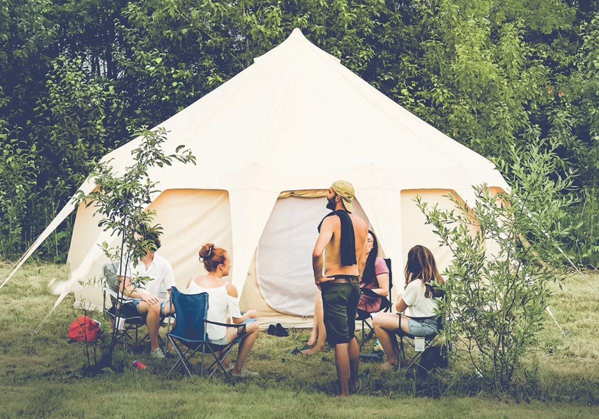 Un petit groupe assis en chaises de camping devant une tente de toile, en forêt